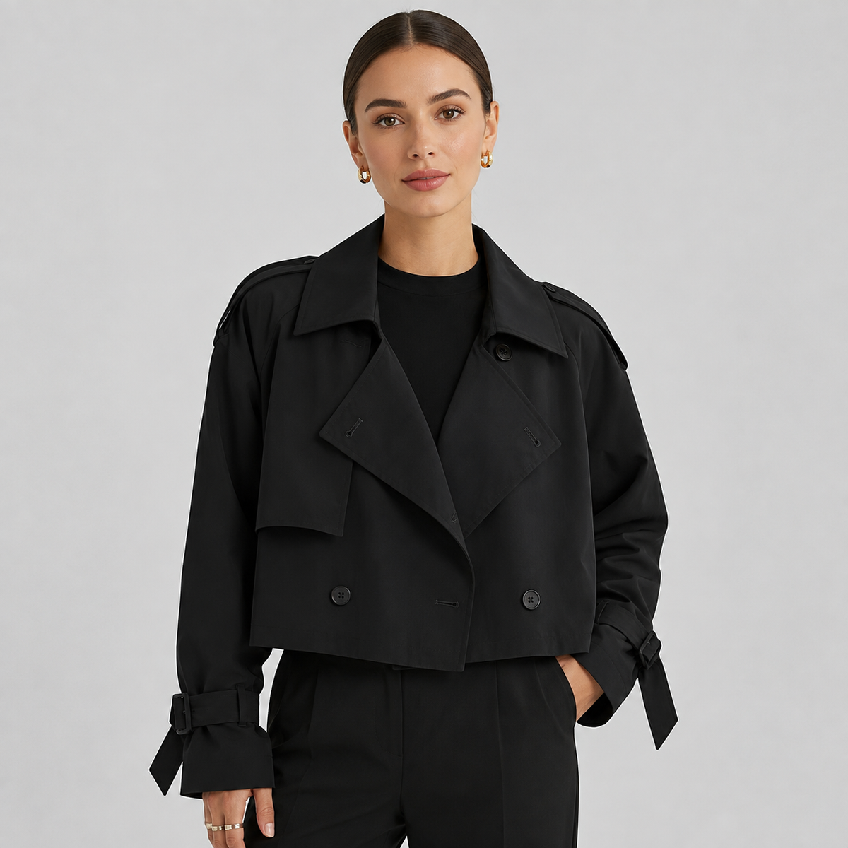 Woman wearing black double breasted cropped trench coat with notch lapels and tie-sleeve cuffs over black t-shirt