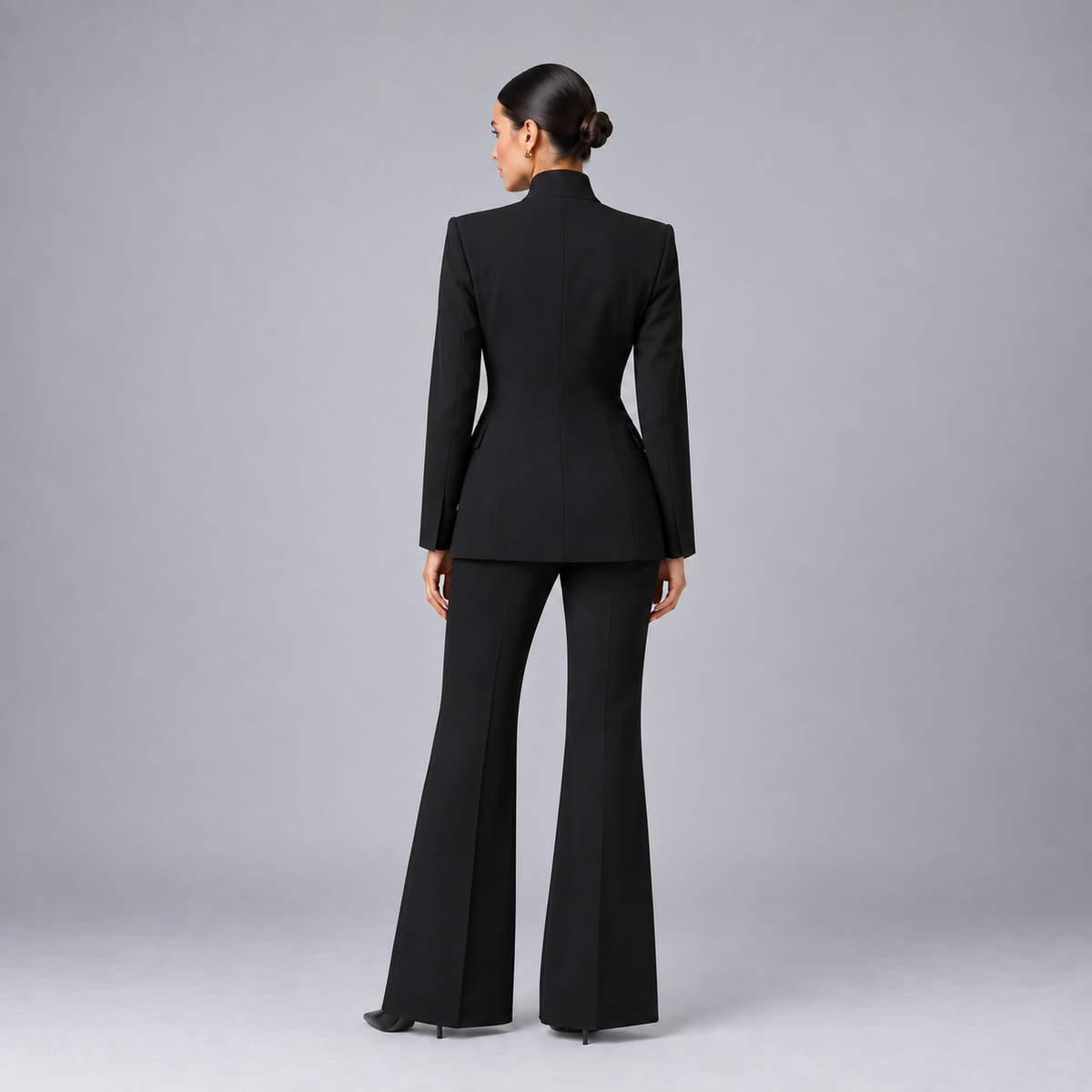 Woman wearing black tailored blazer and wide-leg trousers suit set, viewed from behind against gray background