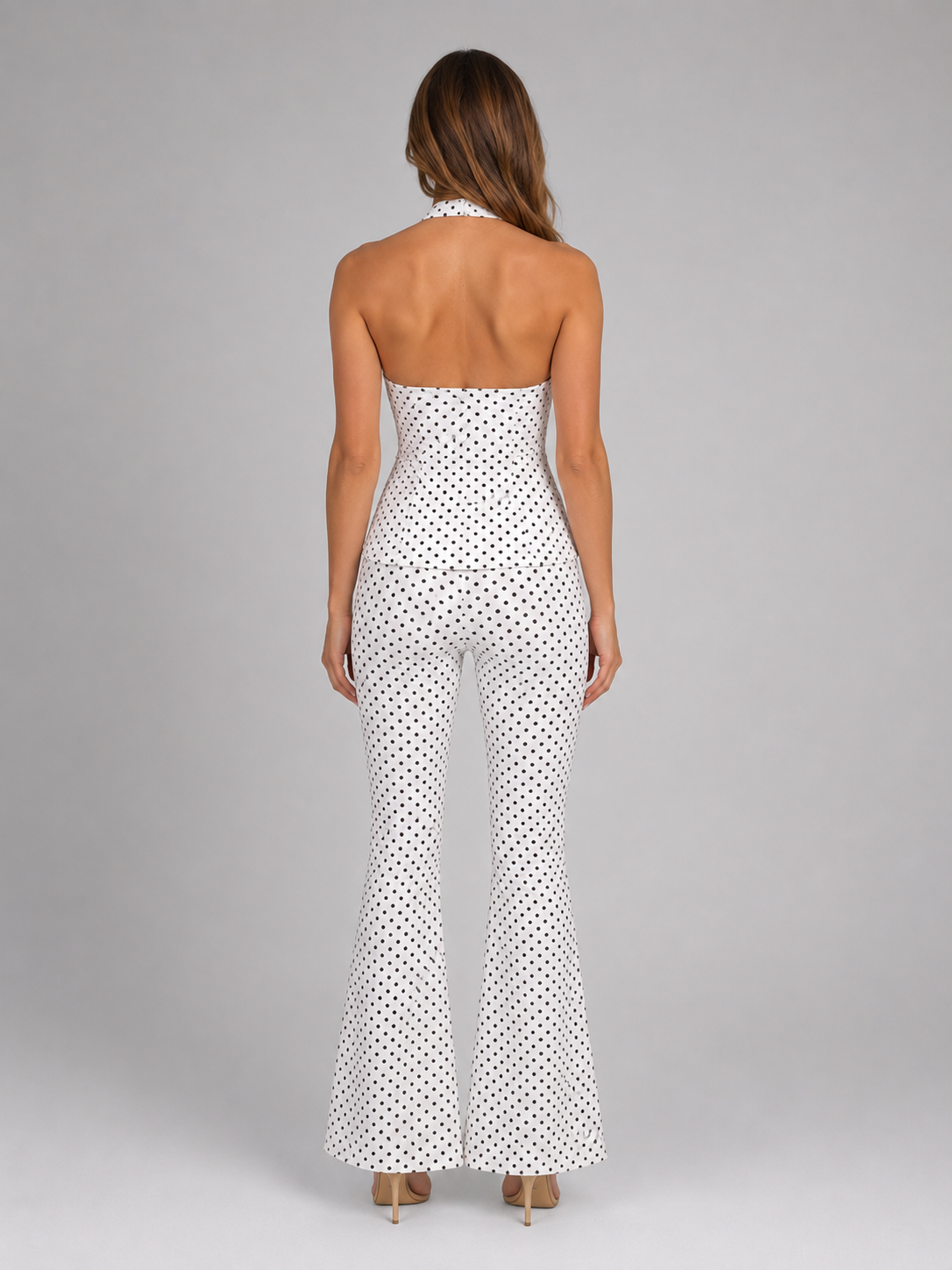 Woman wearing white halter polka dot tank top with matching wide leg trousers, shown from back view against gray background