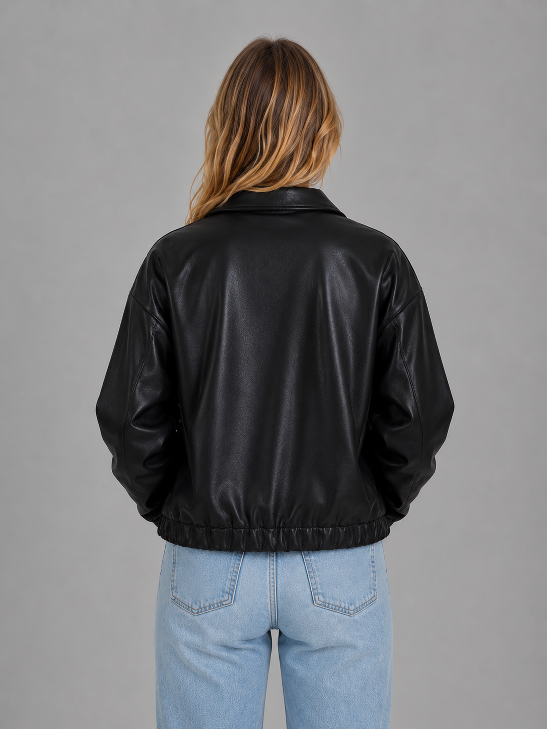 Woman wearing black cropped leather zip jacket with relaxed fit and pockets, paired with light blue jeans, back view