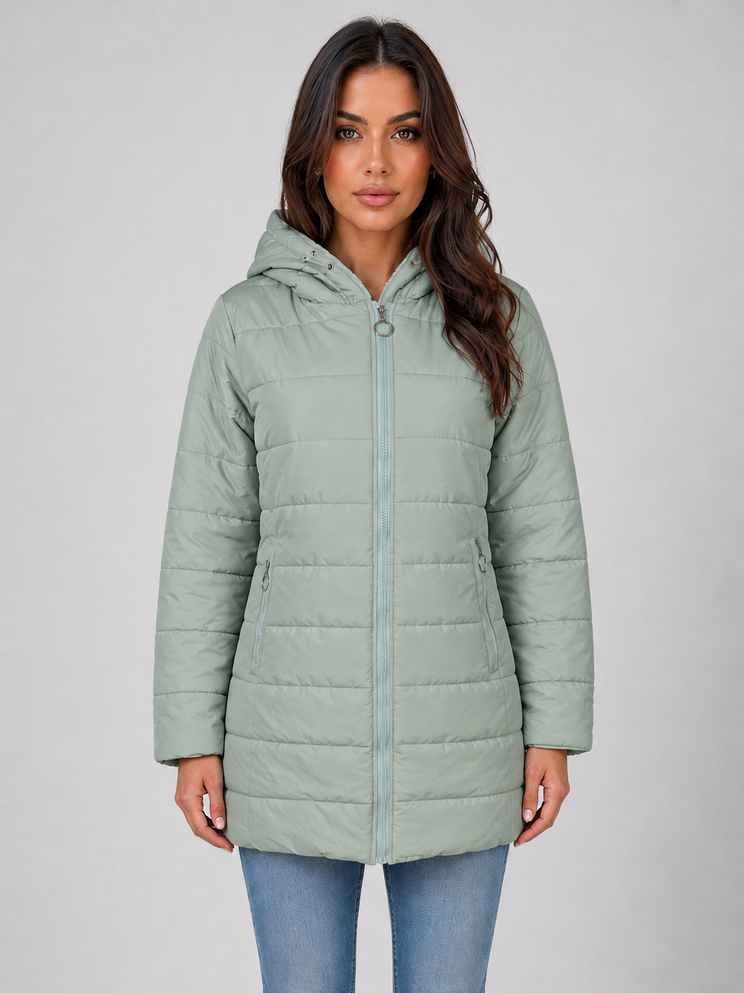Woman wearing sage green hooded quilted puffer jacket with fleece lining over blue jeans against white background