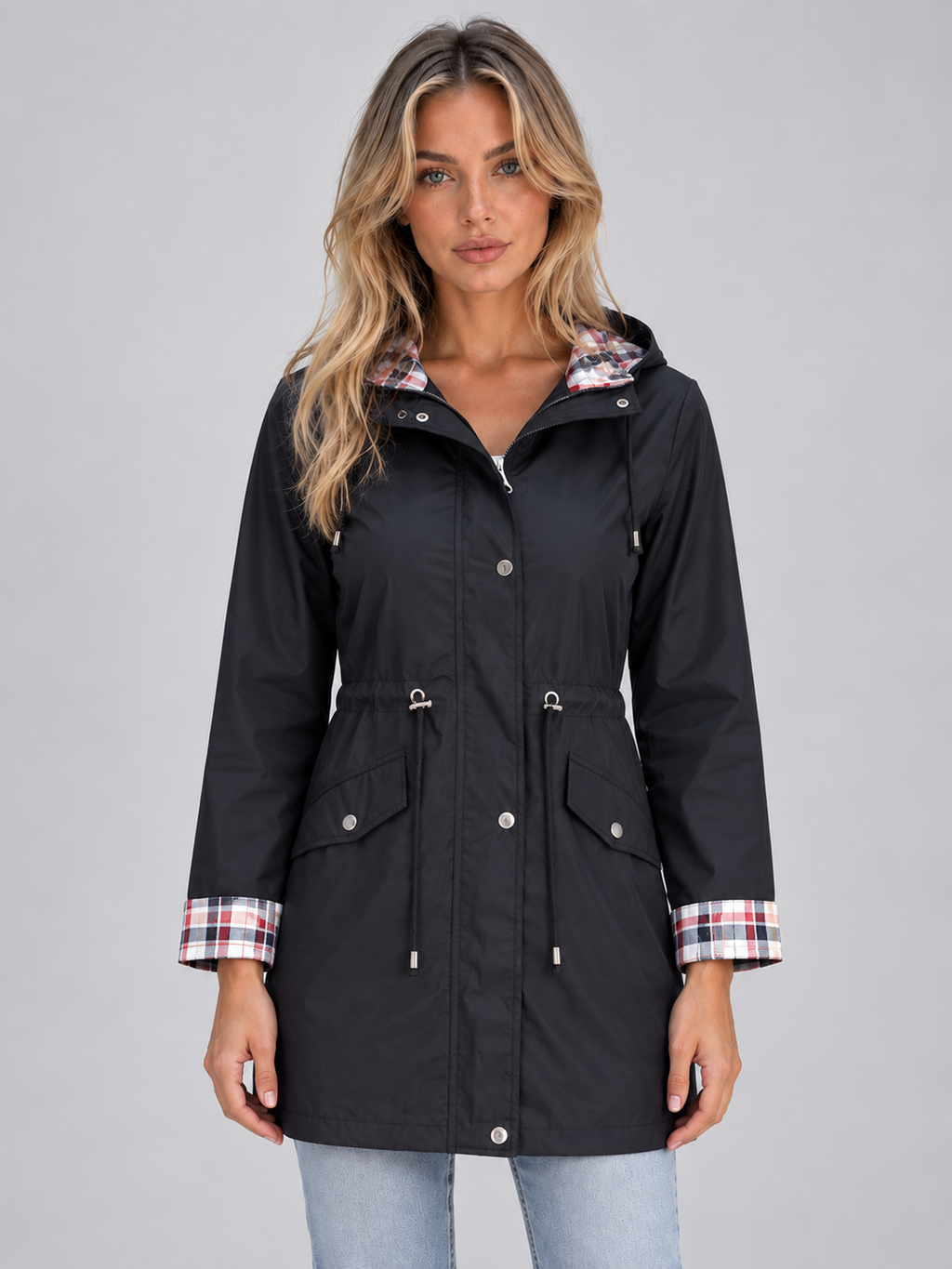 Women's black zip-up hooded raincoat parka with plaid lining, drawstring waist, and chest pockets worn over light blue jeans