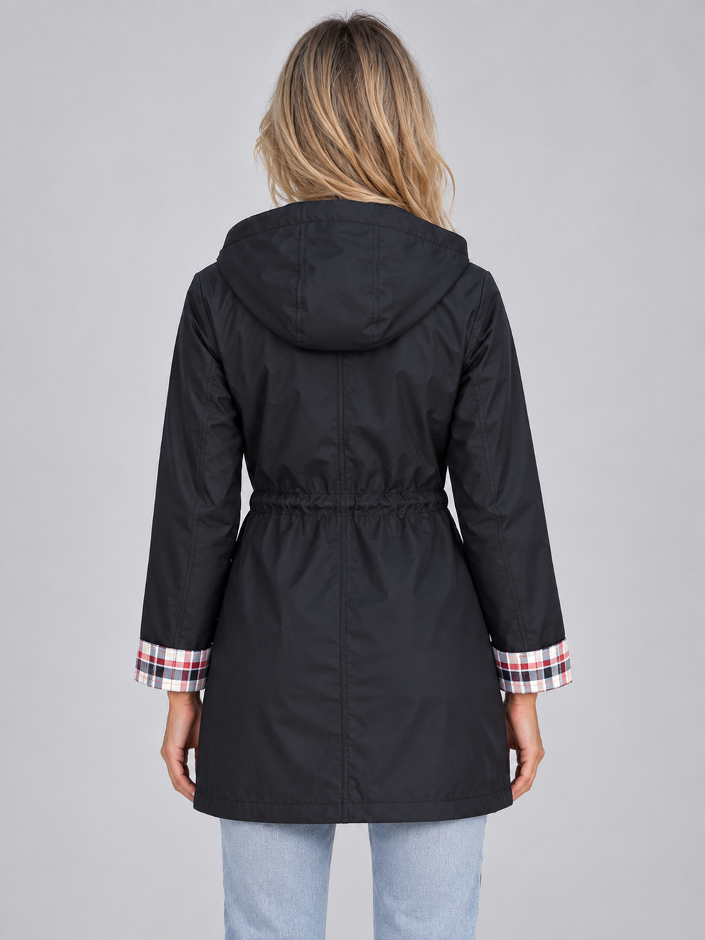 Woman wearing black hooded raincoat parka with plaid trim cuffs and drawstring waist, back view