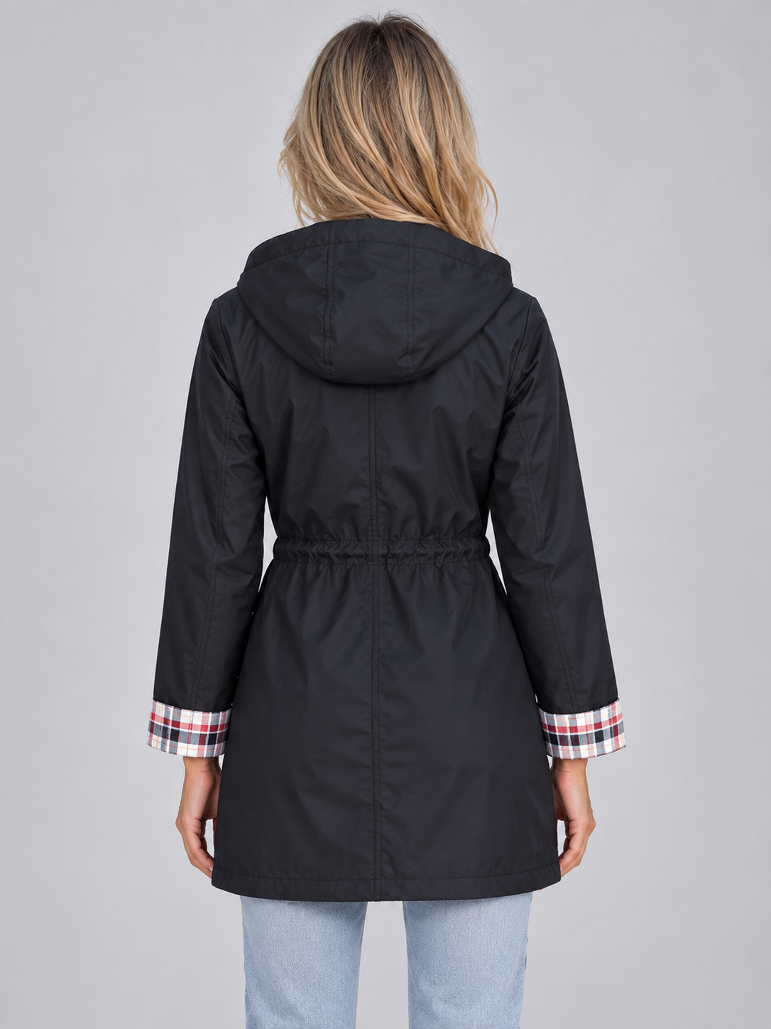 Woman wearing black hooded raincoat parka with plaid trim cuffs and drawstring waist, back view