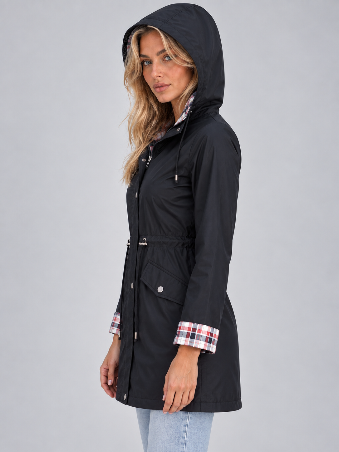 Women's black zip-up hooded raincoat parka with plaid cuff lining and adjustable drawstring waist, styled with light blue jeans