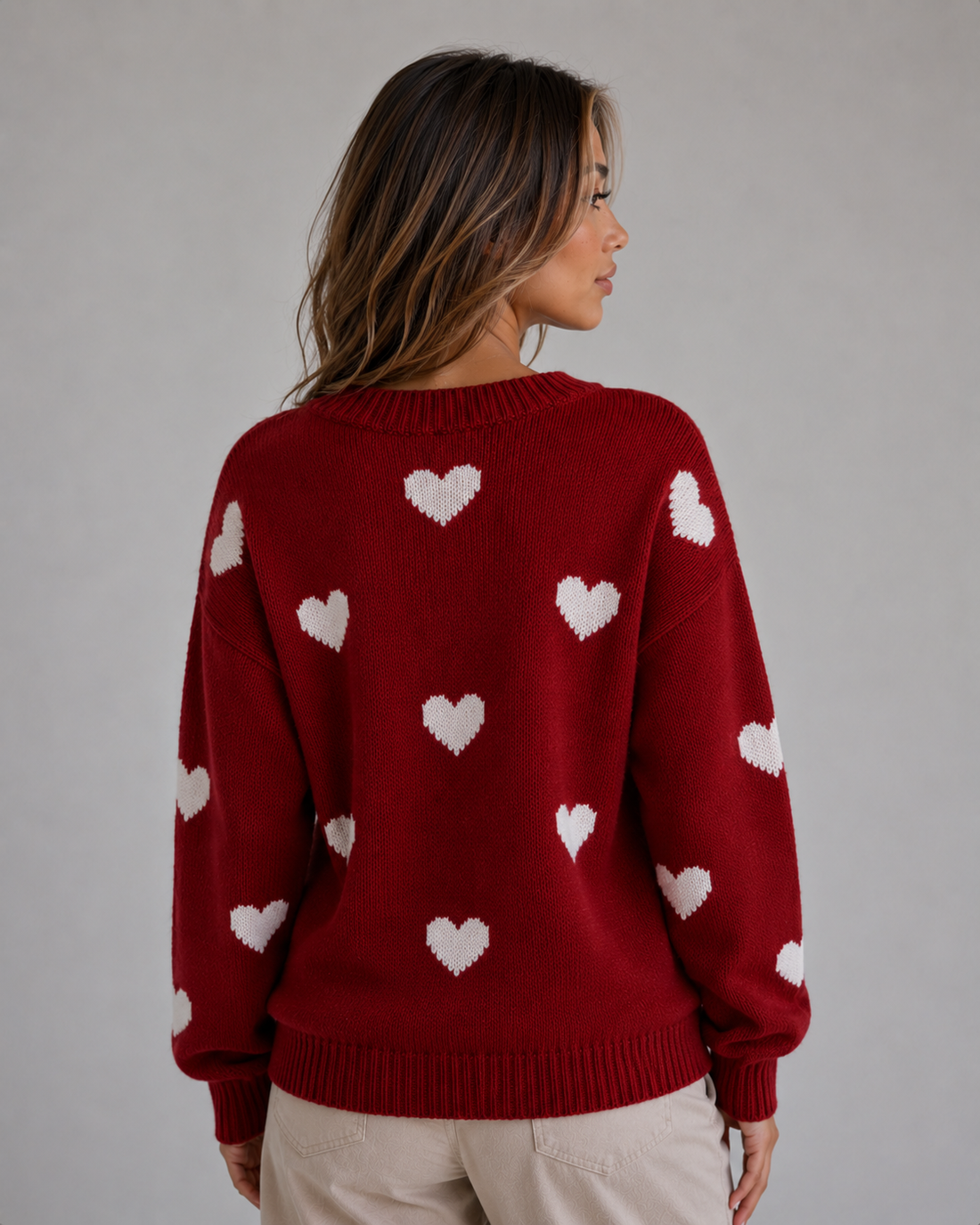 Woman wearing red crew neck knitted jumper with white heart print pattern, shown from back view