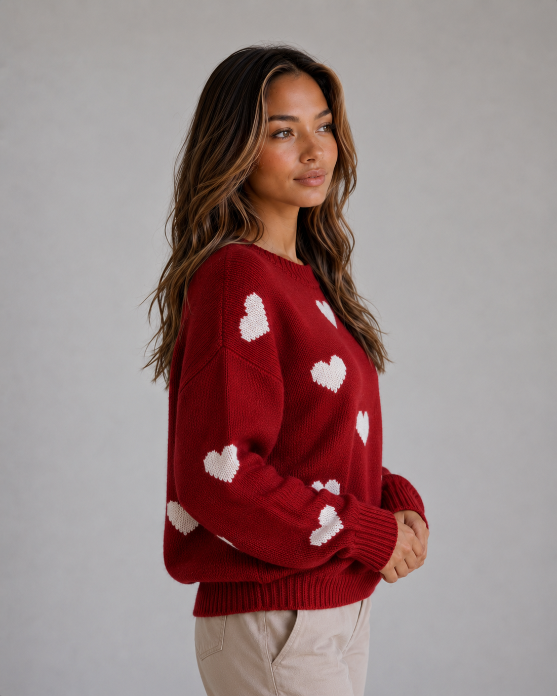 Woman wearing red crew neck sweater with white heart pattern, paired with beige pants