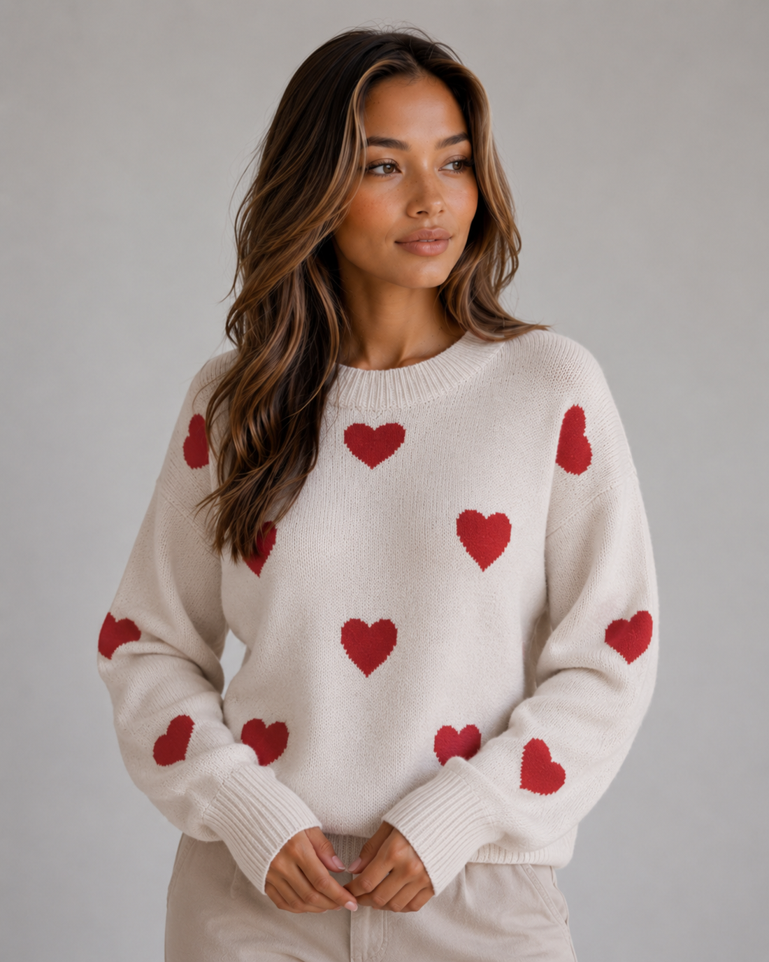 Woman wearing cream crew neck knitted sweater with red heart pattern scattered across front and sleeves