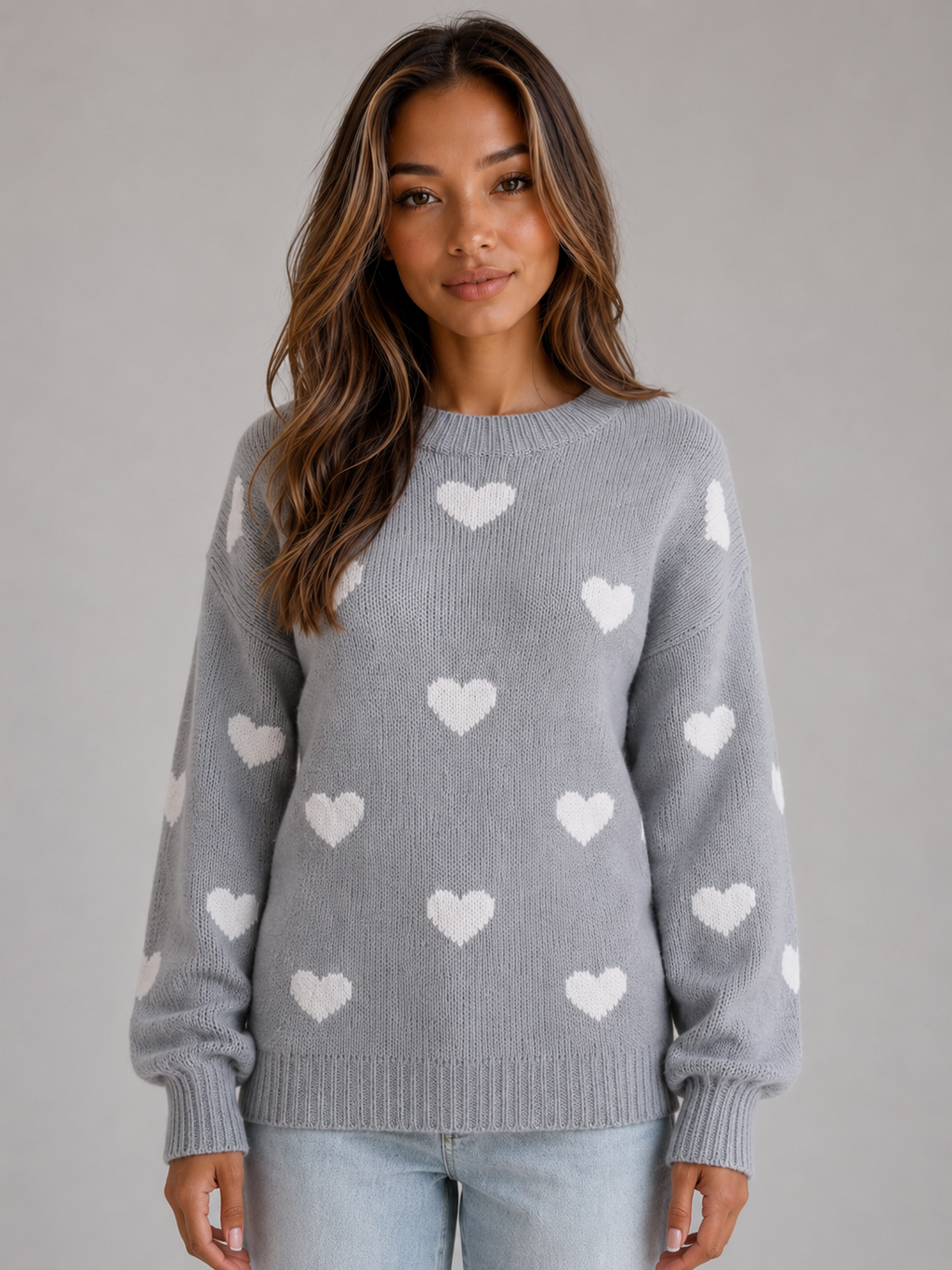 Woman wearing gray crew neck knitted sweater with white heart pattern, paired with light blue jeans