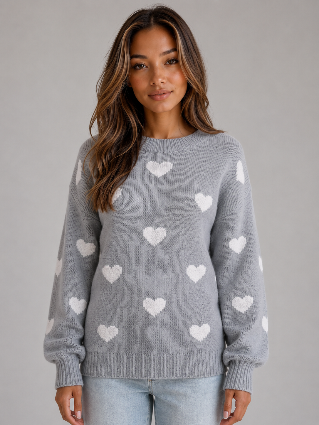 Woman wearing gray crew neck knitted sweater with white heart pattern, paired with light blue jeans