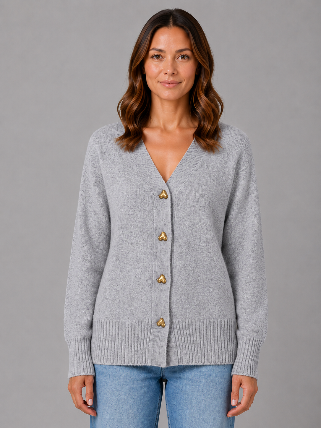 Woman wearing light gray v-neck cardigan with gold heart-shaped buttons and ribbed cuffs over blue jeans
