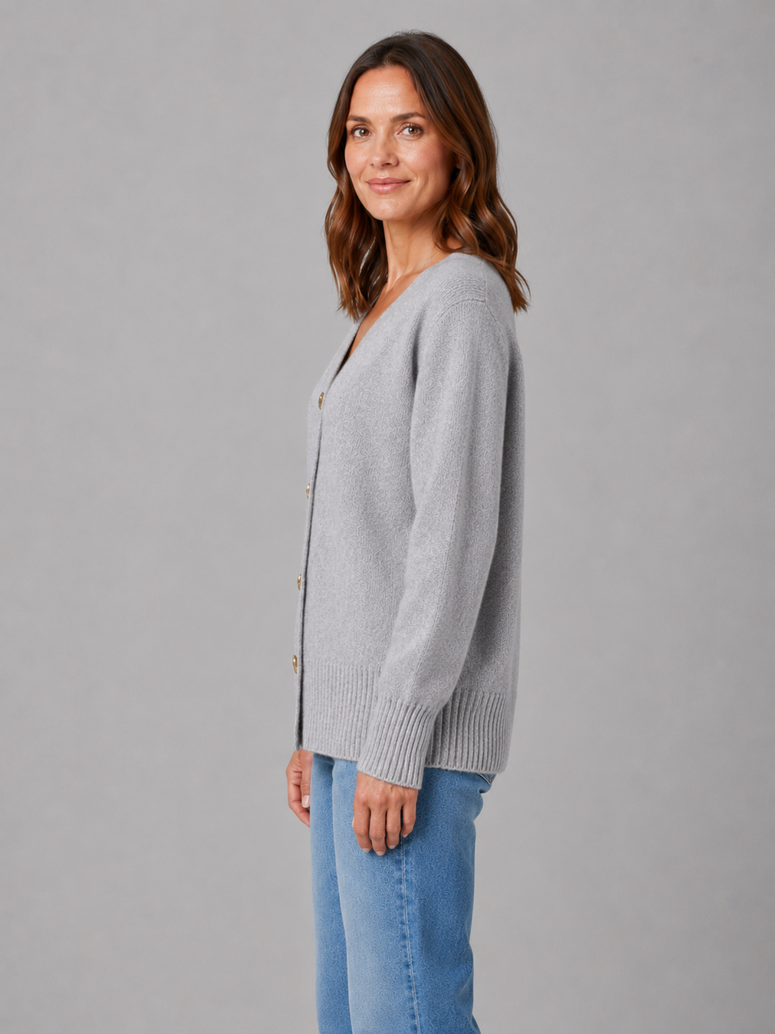 Woman wearing light gray button-up cardigan with heart buttons over blue jeans, side profile view