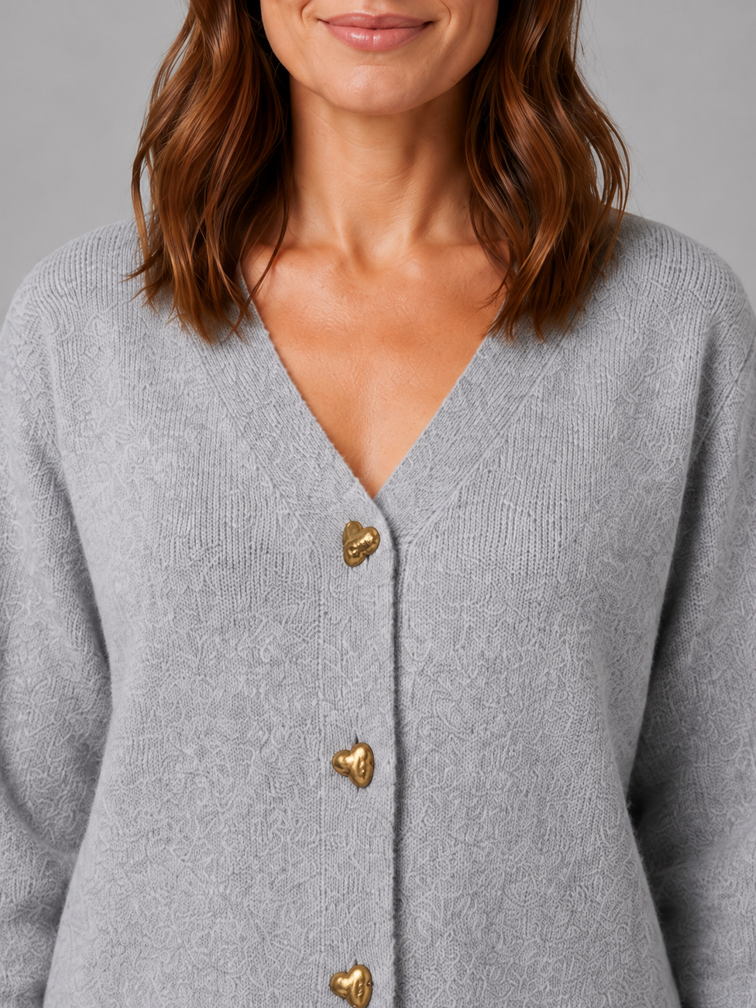 Woman wearing light gray ribbed V-neck cardigan with gold heart-shaped buttons