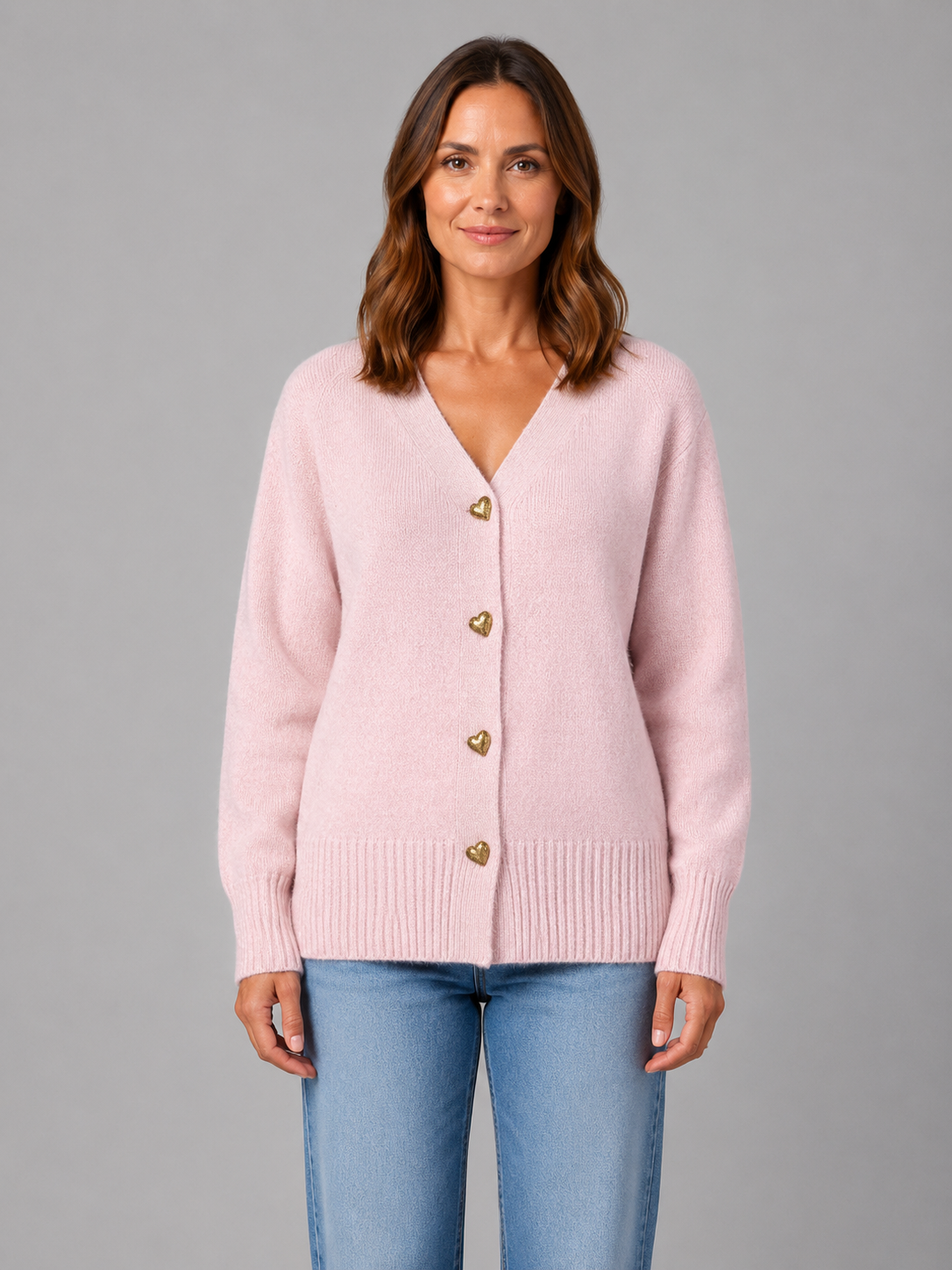 Woman wearing pink soft knit cardigan with heart-shaped gold buttons and V-neckline, paired with light blue jeans