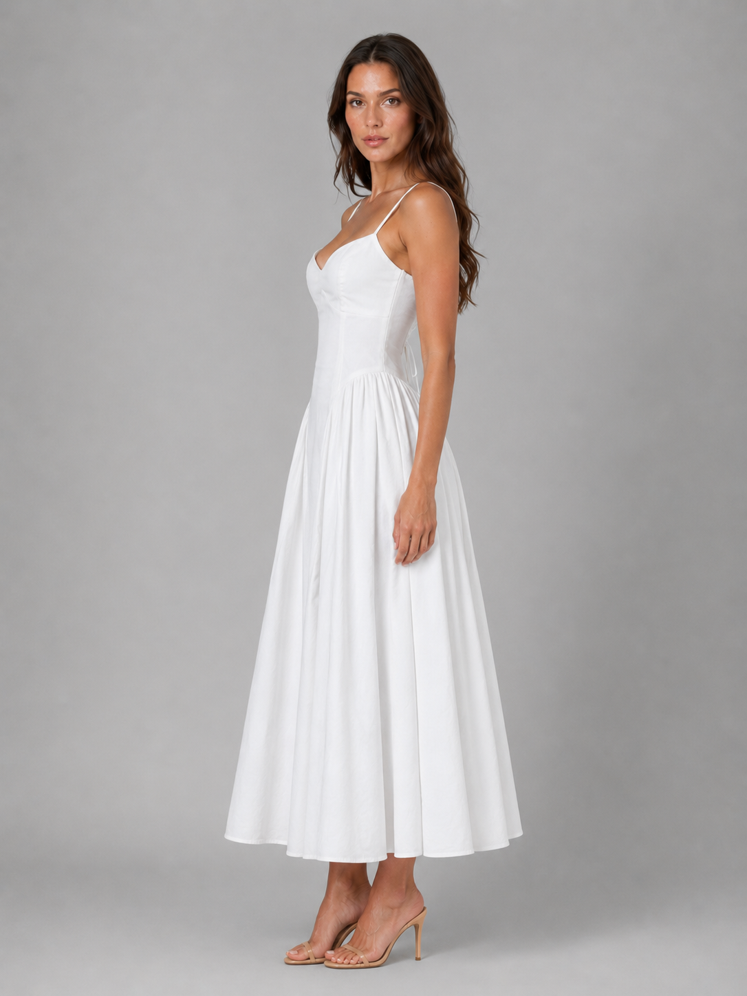 Woman wearing white sleeveless corset midi dress with full skirt and thin straps, styled with nude heels