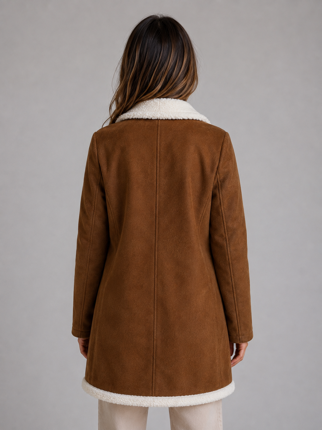 Woman wearing brown suede longline coat with white shearling collar and hem trim, back view