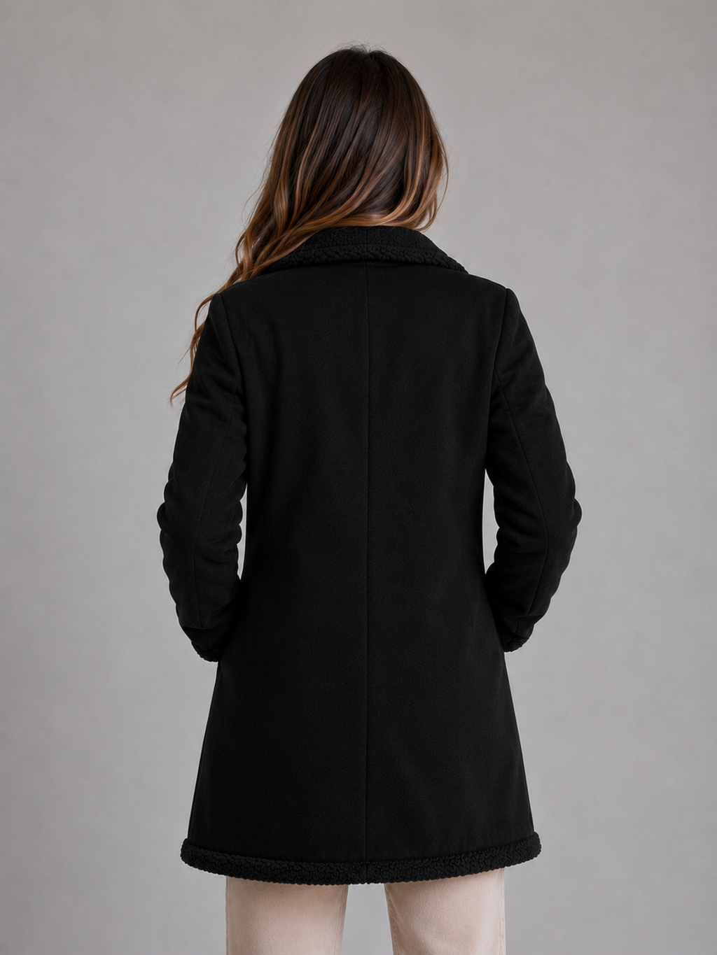 Woman wearing black longline shearling suede coat with teddy trim collar and hem, shown from back view