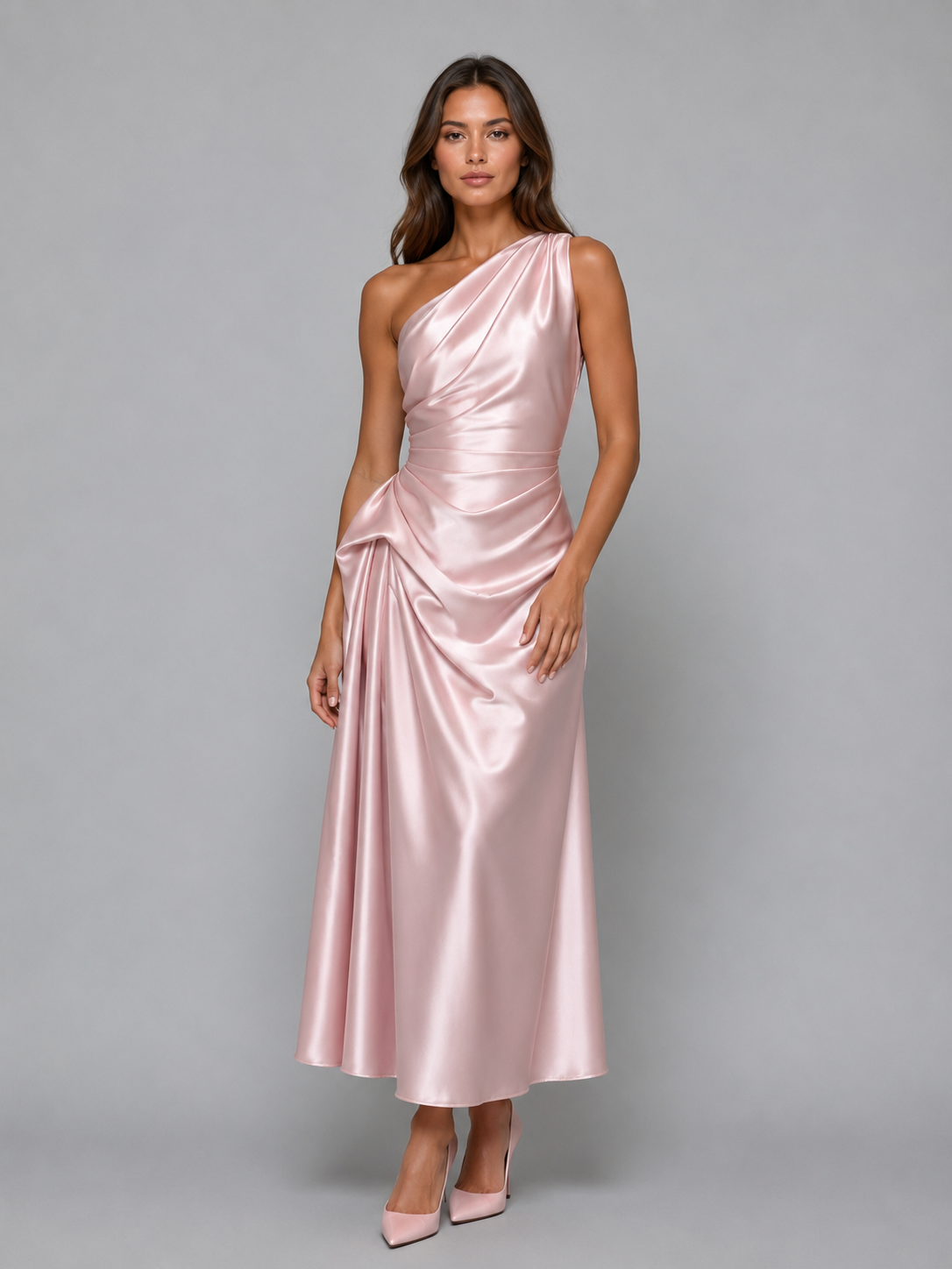 Woman wearing pink one-shoulder ruched satin evening midi dress with matching heels on gray background