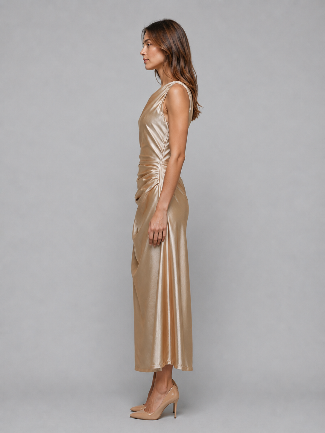 Woman wearing champagne satin one-shoulder ruched midi dress with nude heels, side profile view