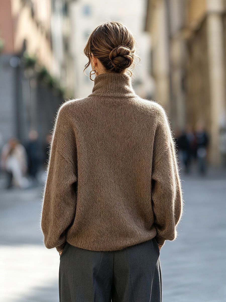 Woman wearing beige oversized mohair-blend turtleneck sweater with dark trousers, viewed from back on urban street