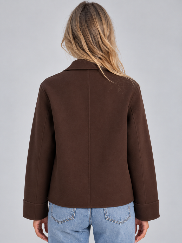 Woman wearing brown button-up collared overshirt jacket with patch pockets over light blue jeans, back view