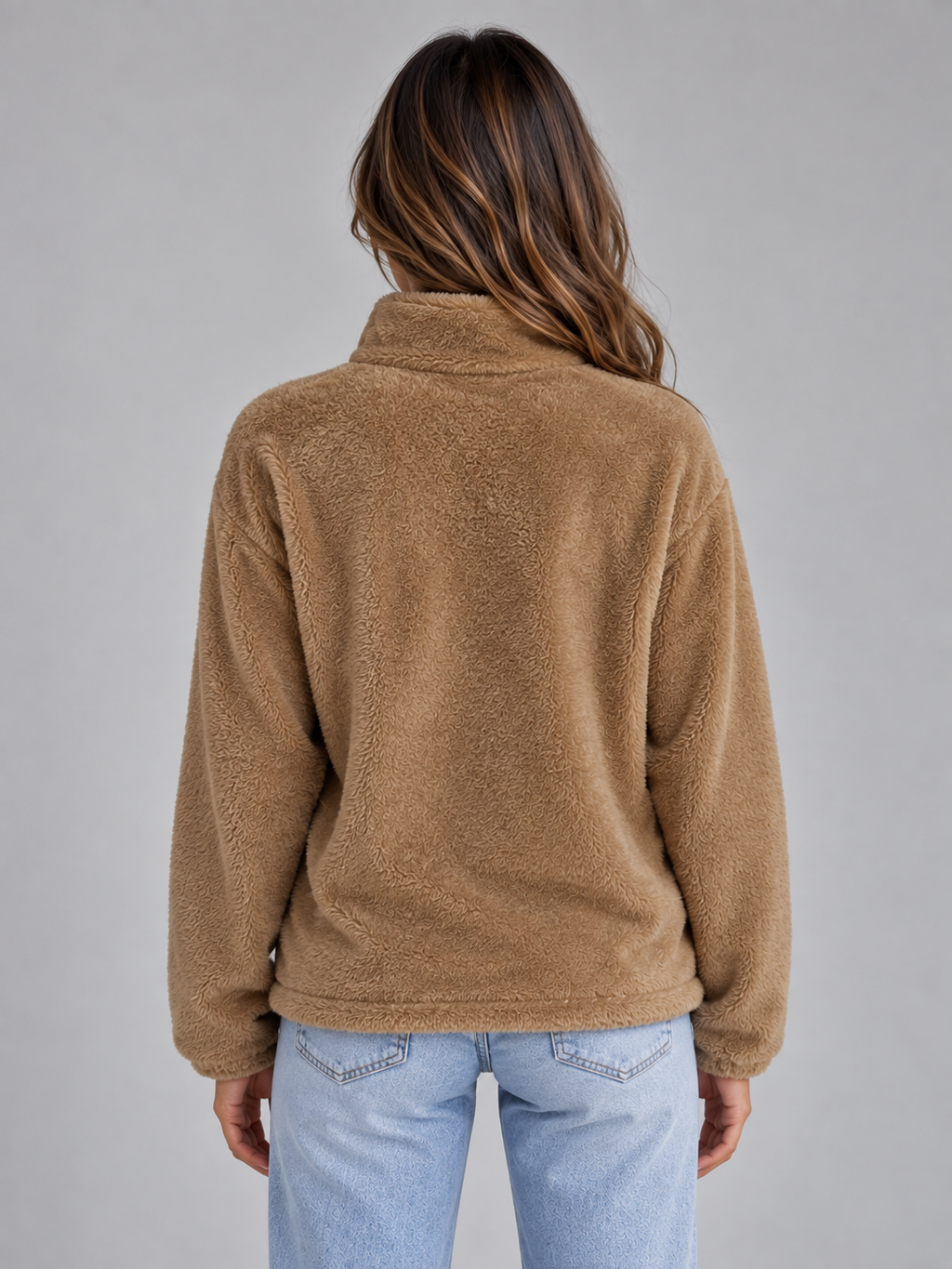 Woman wearing camel colored high neck zip-up teddy fleece jacket over light blue jeans, back view