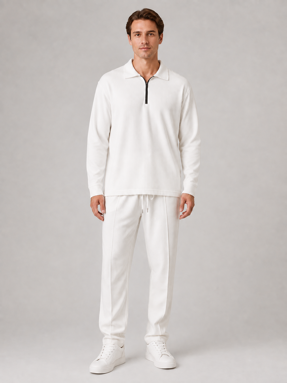 Man wearing white quarter-zip polo shirt and textured white trousers with white sneakers on neutral background