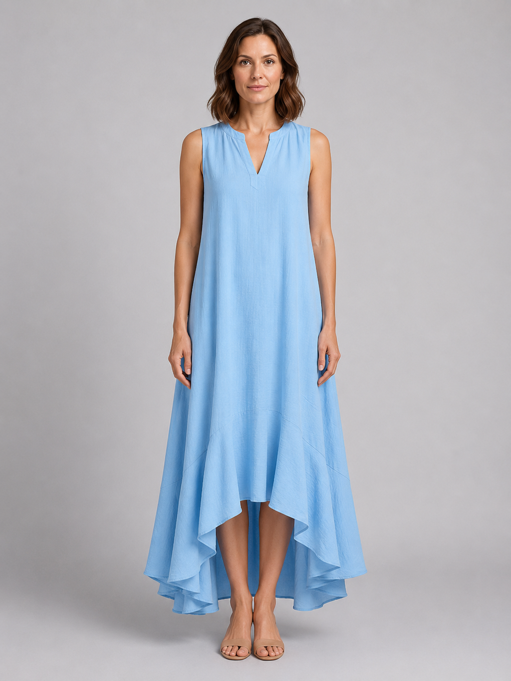 Woman wearing light blue sleeveless v-neck maxi dress with asymmetrical hemline and flowing fabric, standing against neutral background
