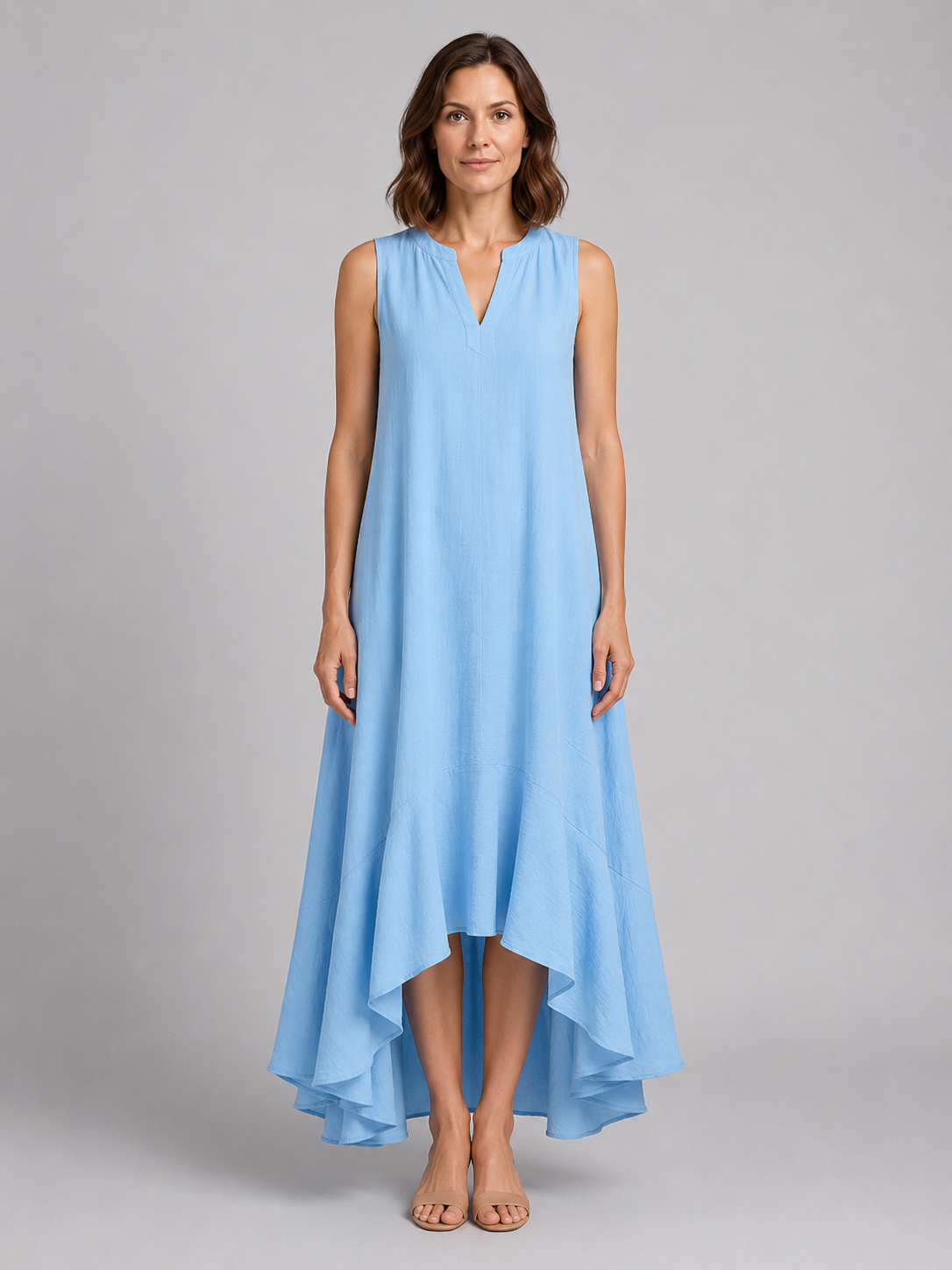 Woman wearing light blue sleeveless v-neck maxi dress with asymmetrical hemline and flowing fabric, standing against neutral background