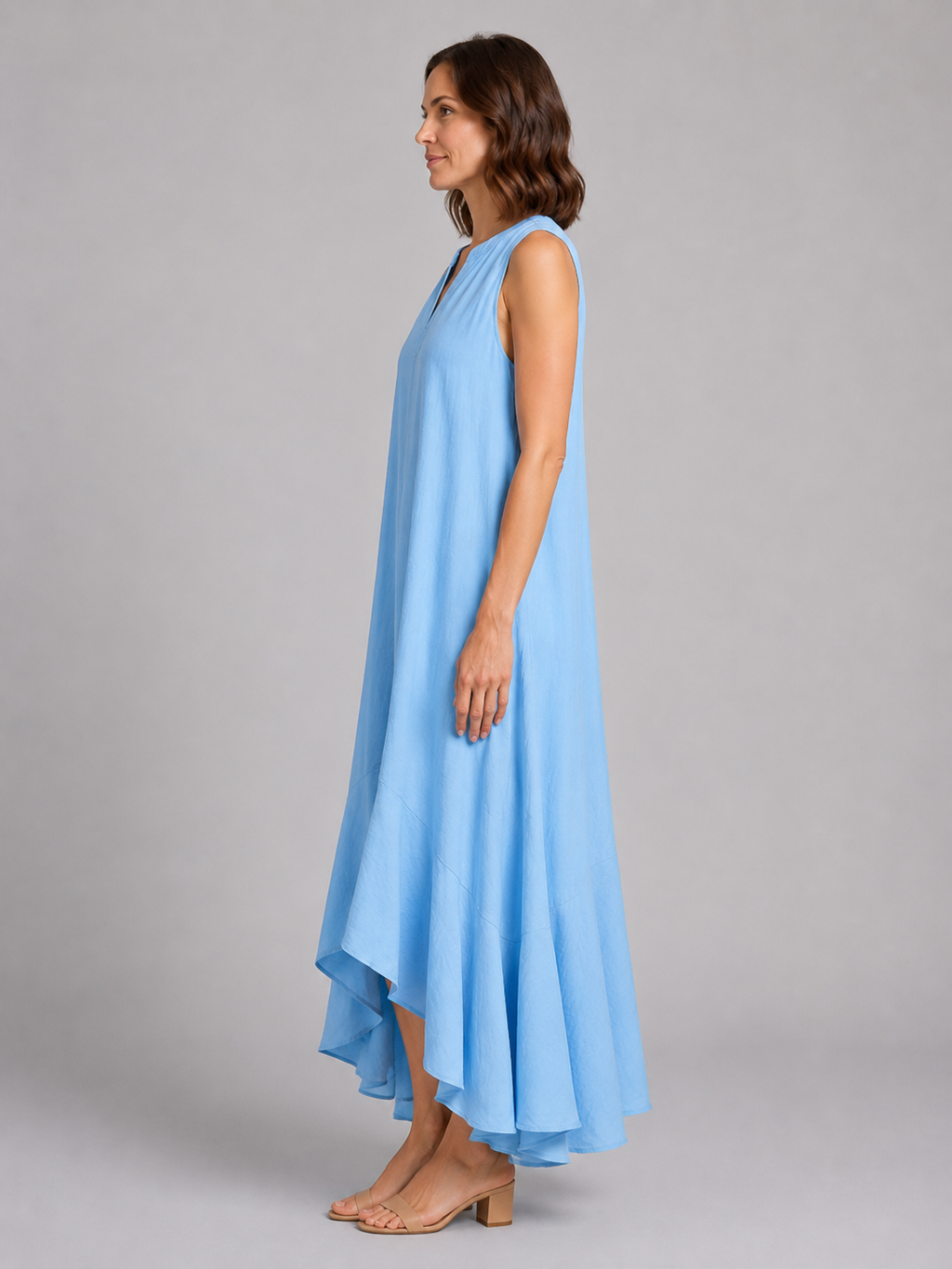 Woman wearing light blue sleeveless V-neck flowy maxi dress with asymmetrical hem and tan block heel sandals