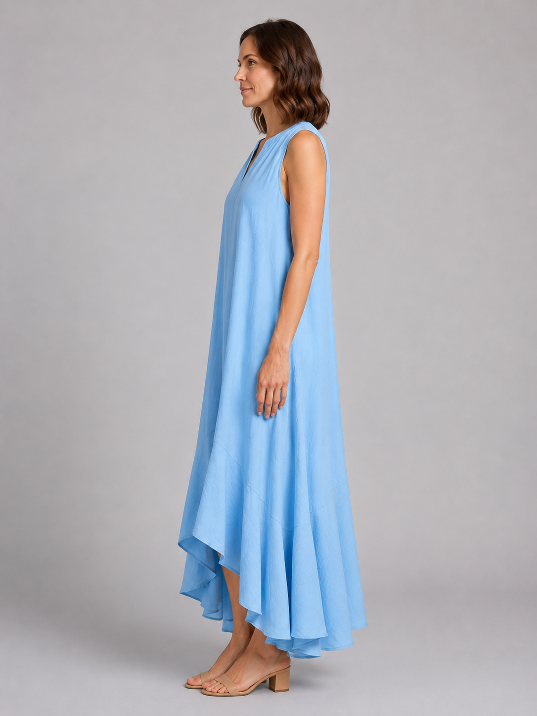 Woman wearing light blue sleeveless V-neck flowy maxi dress with asymmetrical hem and tan block heel sandals