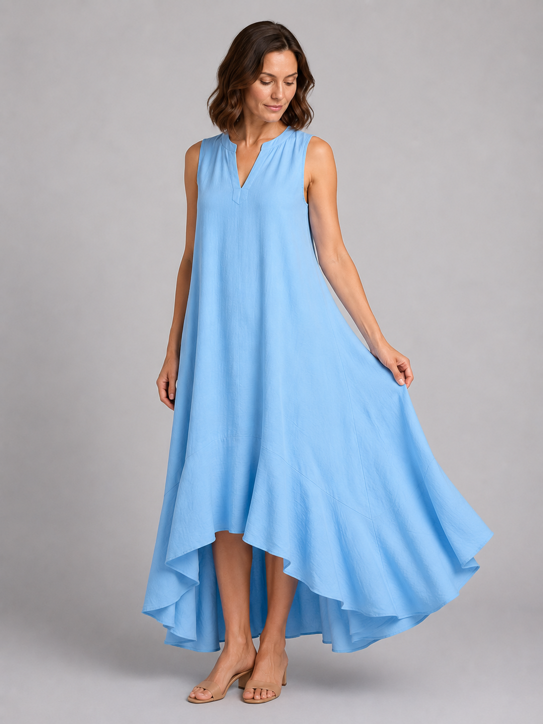 Woman wearing light blue sleeveless V-neck maxi dress with asymmetrical hemline and flowy fit, standing against neutral background