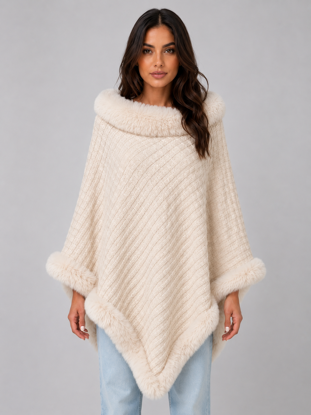 Woman wearing cream ribbed knit poncho with faux fur collar and cuff trim over light blue jeans