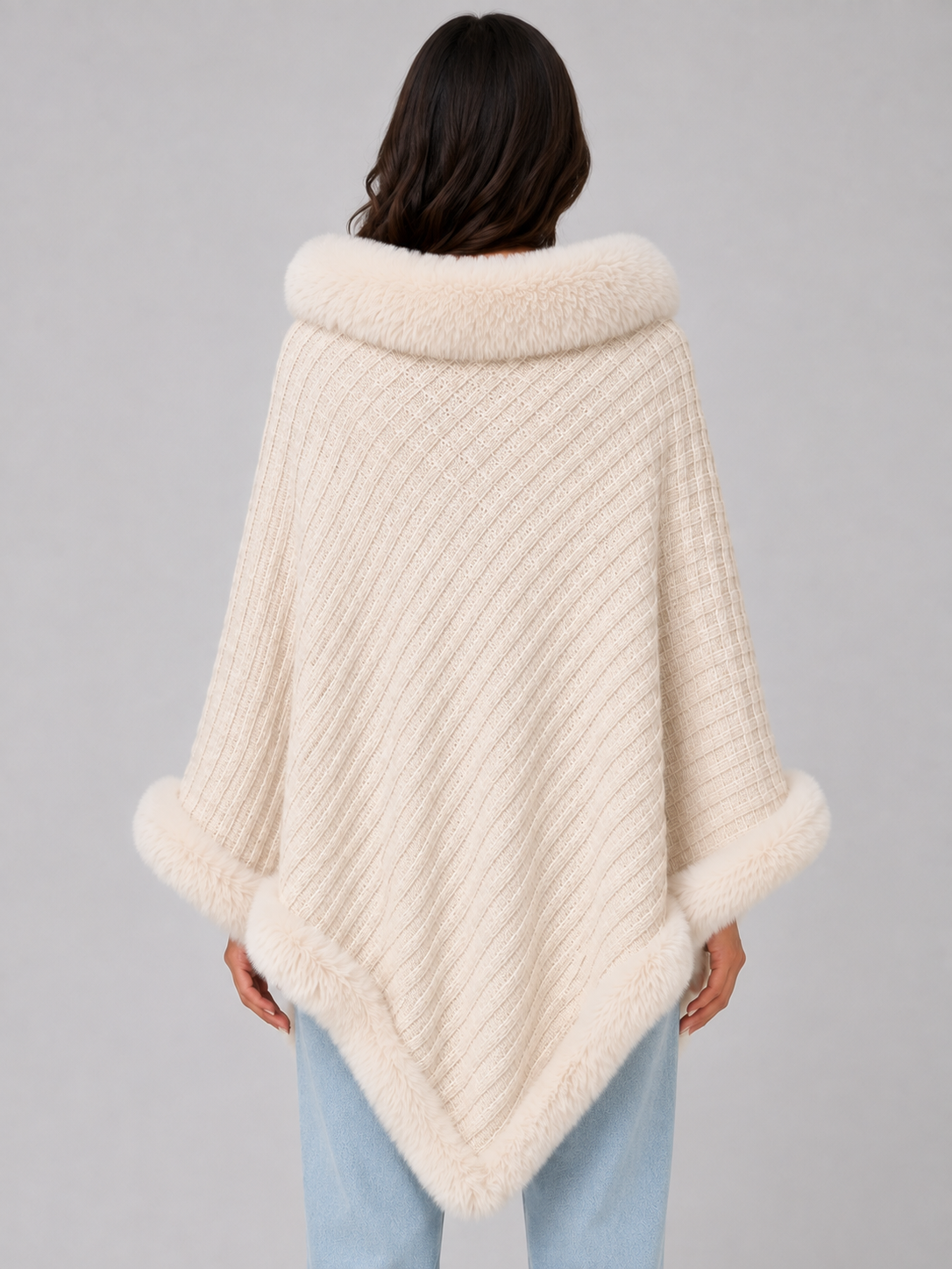 Women's cream knitted cape with faux fur trim collar and hem, worn over light blue jeans, shown from back