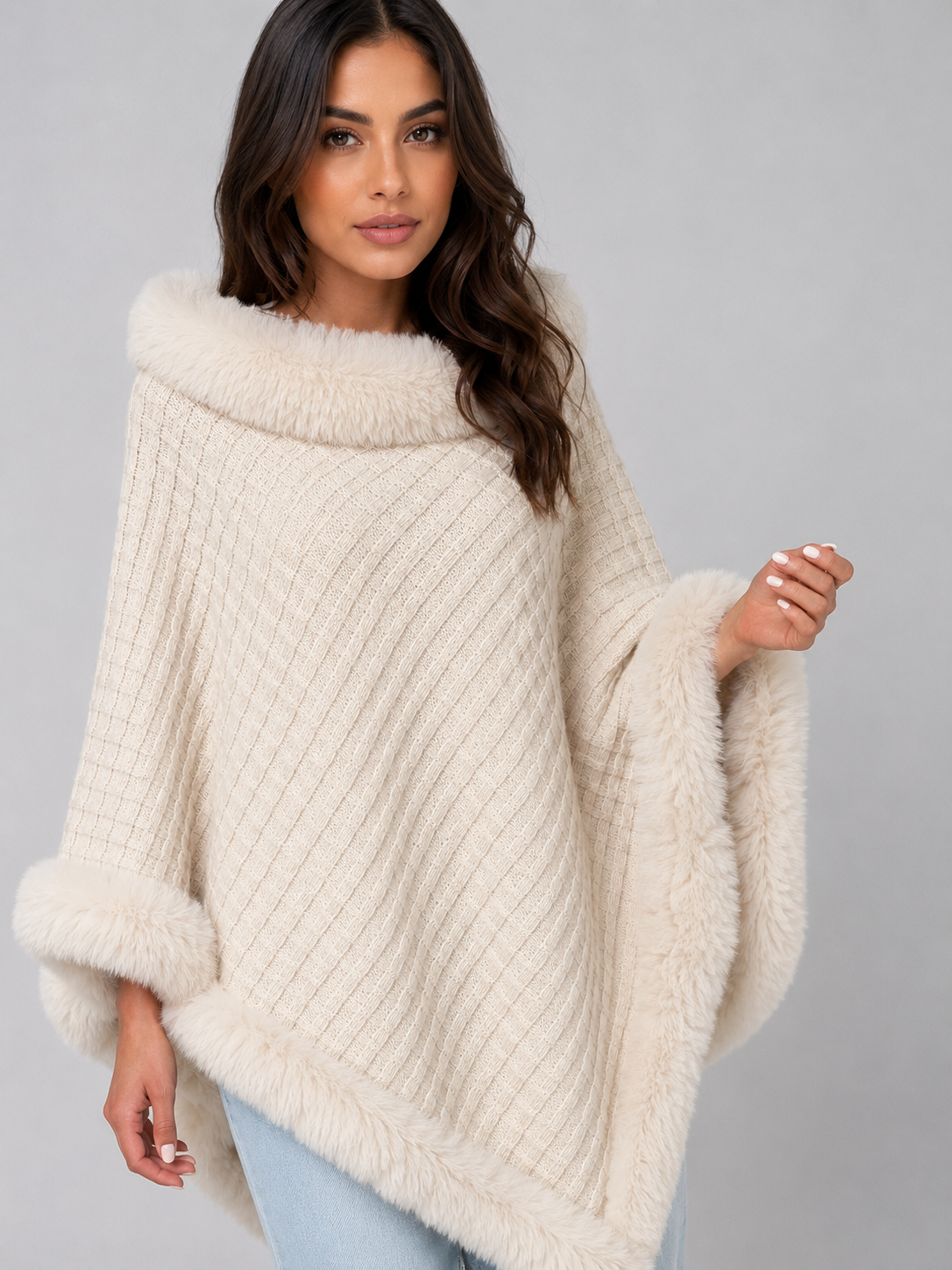 Woman wearing cream ribbed knit poncho with faux fur trim collar, cuffs and hem, paired with light blue jeans