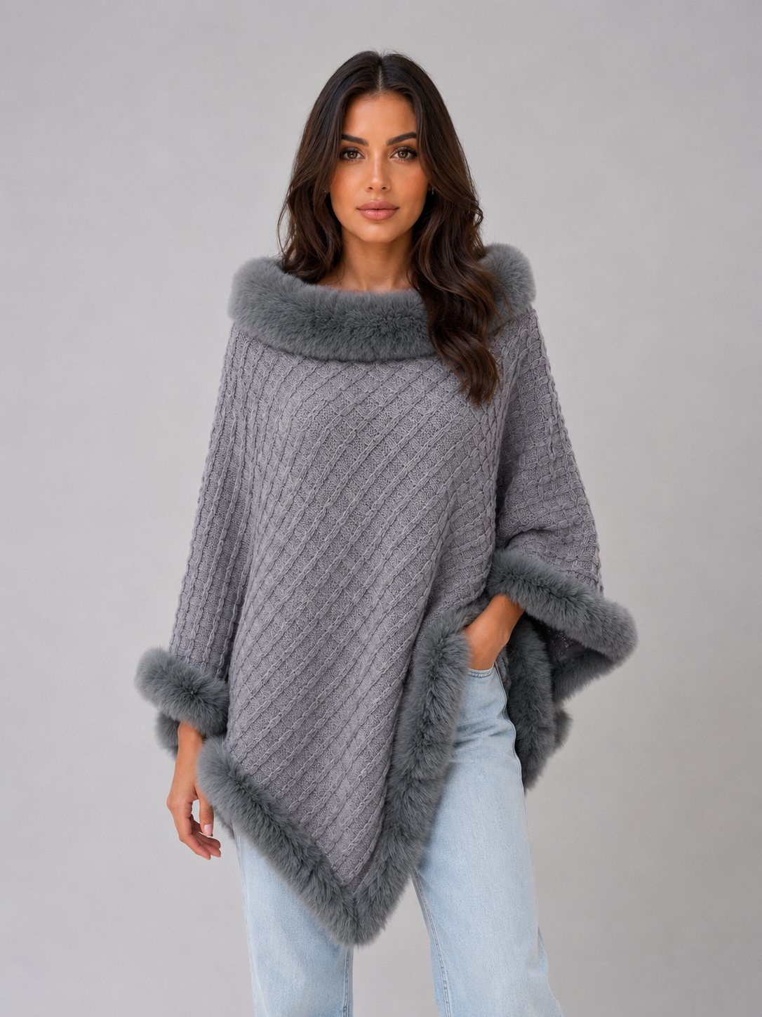 Woman wearing gray ribbed knit poncho with faux fur trim at collar, cuffs and hem, styled with light blue jeans