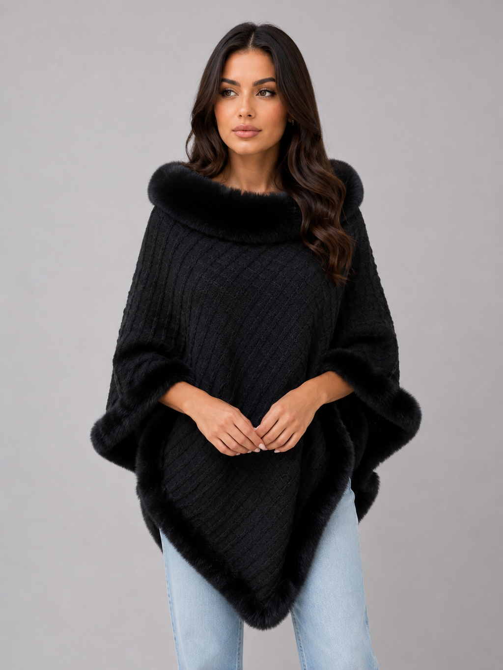 Woman wearing black knitted cape poncho with faux fur trim collar and cuffs over light blue jeans