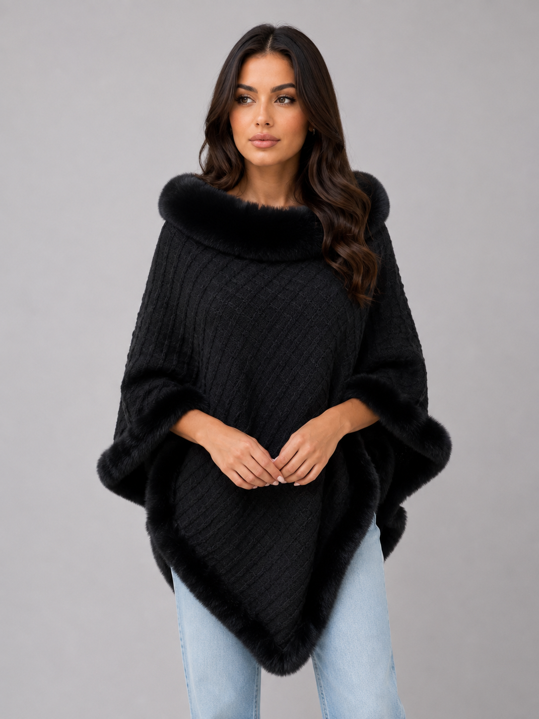 Woman wearing black knitted cape poncho with faux fur trim collar and cuffs over light blue jeans