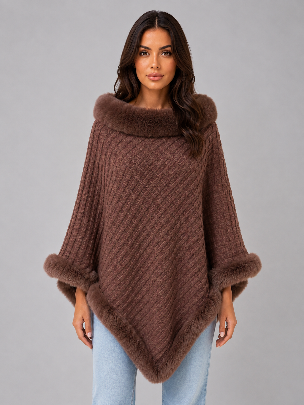 Women's brown knitted cape poncho with faux fur trim collar and cuffs, styled with light blue jeans