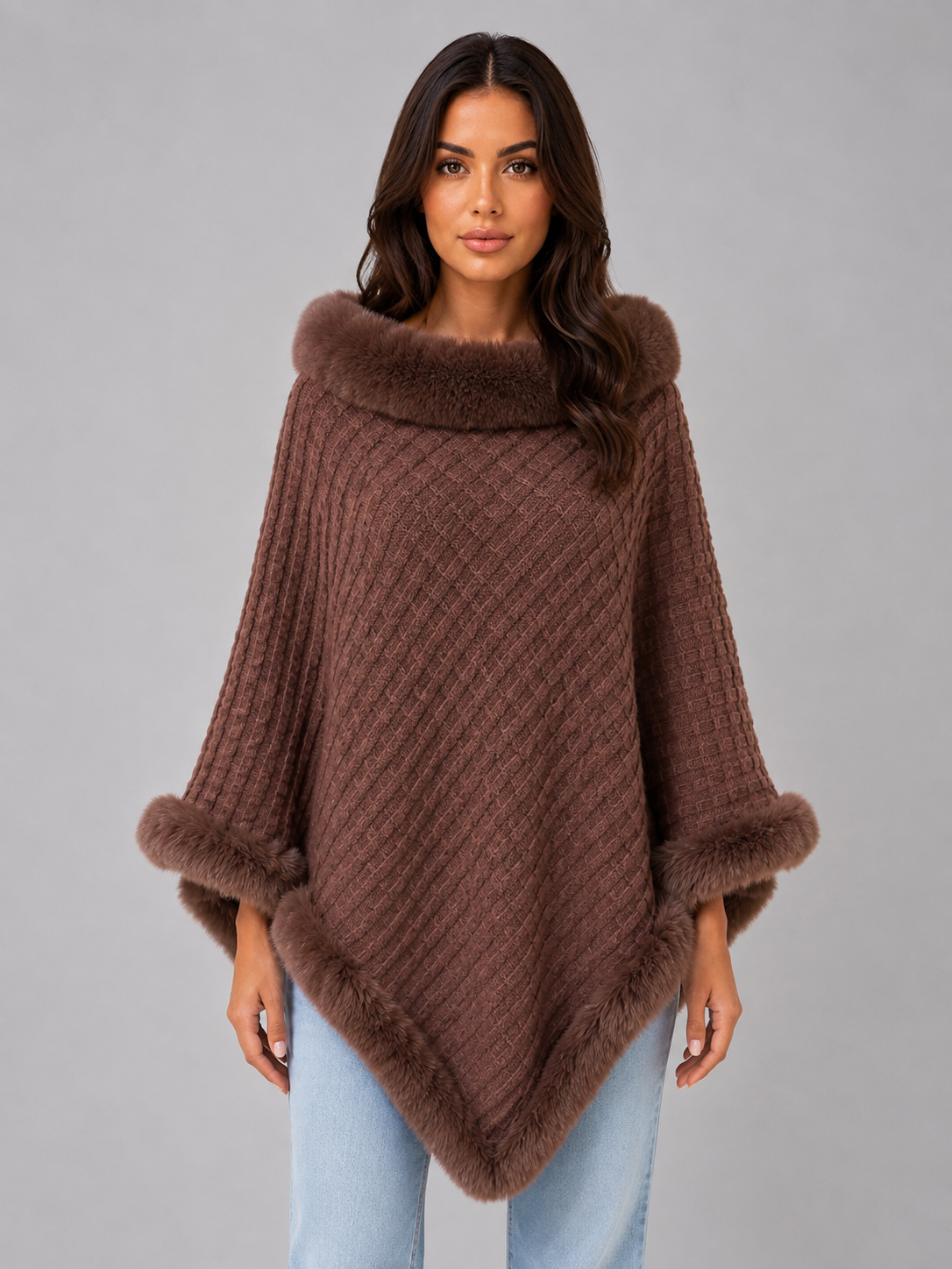 Women's brown knitted cape poncho with faux fur trim collar and cuffs, styled with light blue jeans