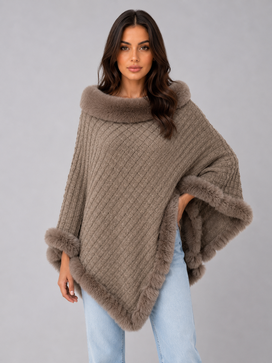 Woman wearing beige knitted poncho with faux fur trim collar and hem, paired with light blue jeans