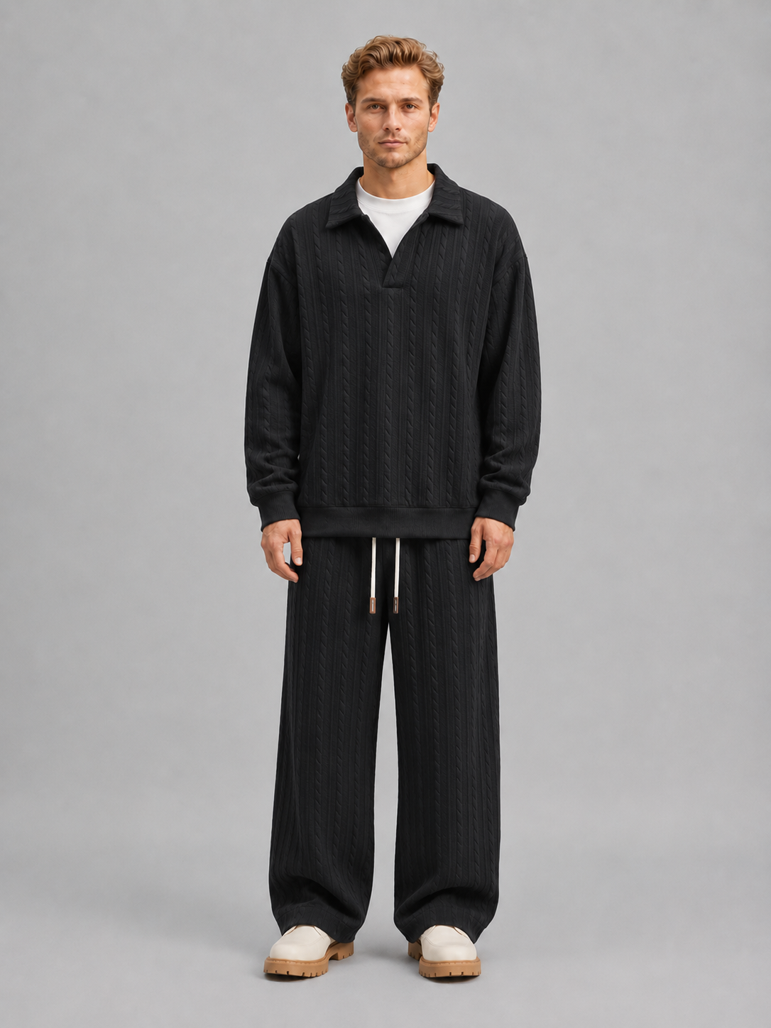 Man wearing black cable knit collared sweater and matching wide-leg trousers with drawstring waist, styled with cream chunky platform shoes