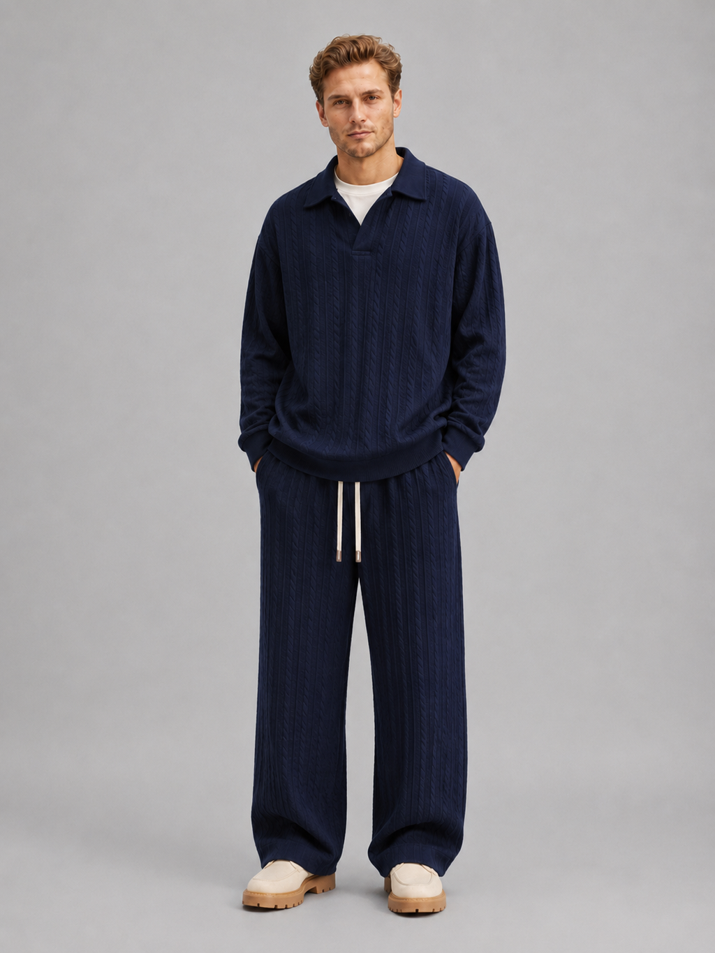 Man wearing navy cable knit collared pullover and matching wide-leg trousers with drawstring waist, styled with cream platform slides