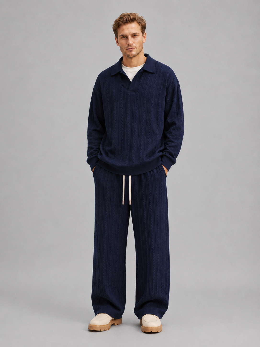 Man wearing navy cable knit collared pullover and matching wide-leg trousers with drawstring waist, styled with cream platform slides