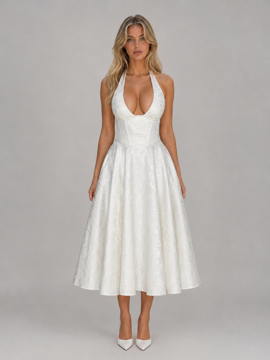 Woman wearing white jacquard halter midi dress with full skirt and white pointed-toe heels against gray background