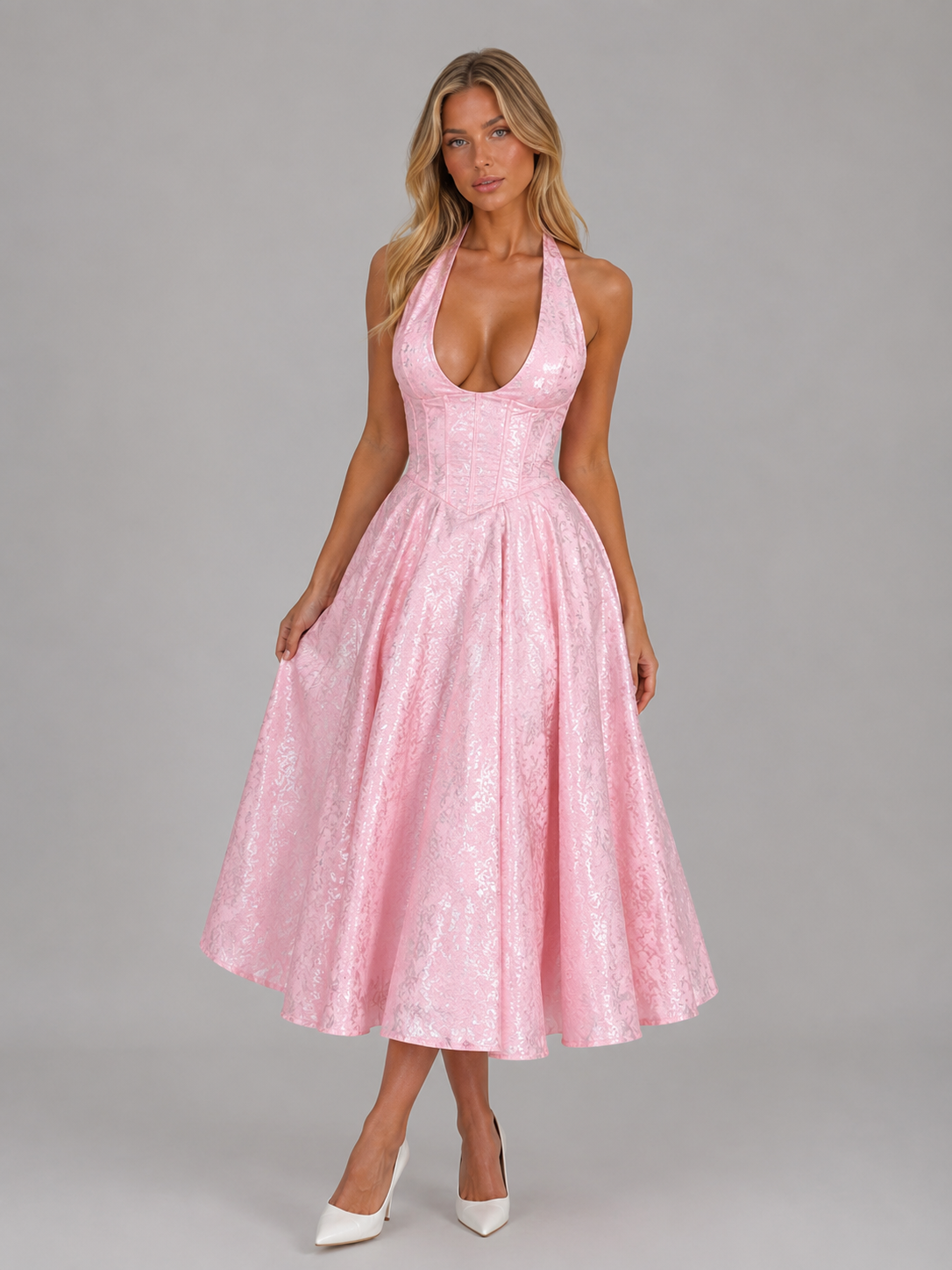 Woman wearing pink jacquard halter midi dress with full skirt and white heels against gray background