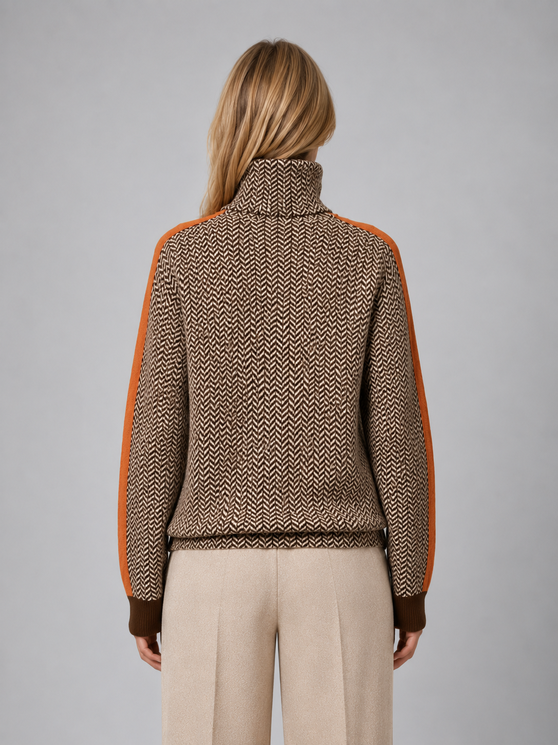 Woman wearing brown herringbone turtleneck jumper with orange sleeves and cream pants, back view