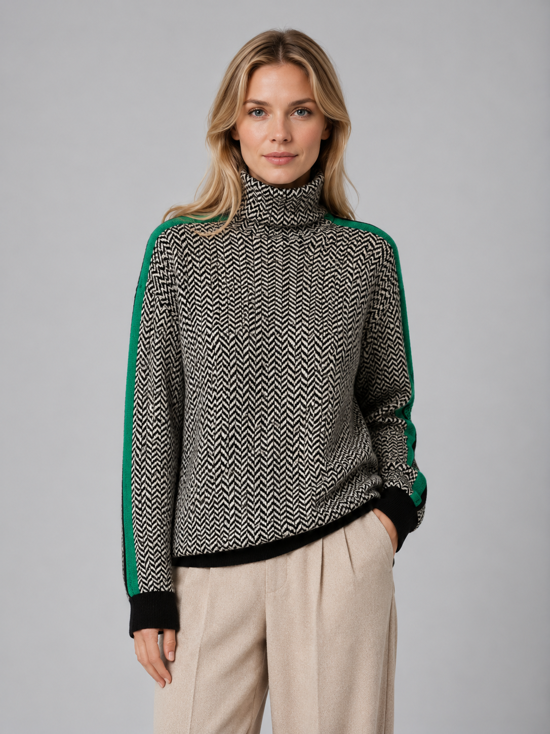 Woman wearing cream herringbone turtleneck sweater with green side stripes and black cuffs over beige pants