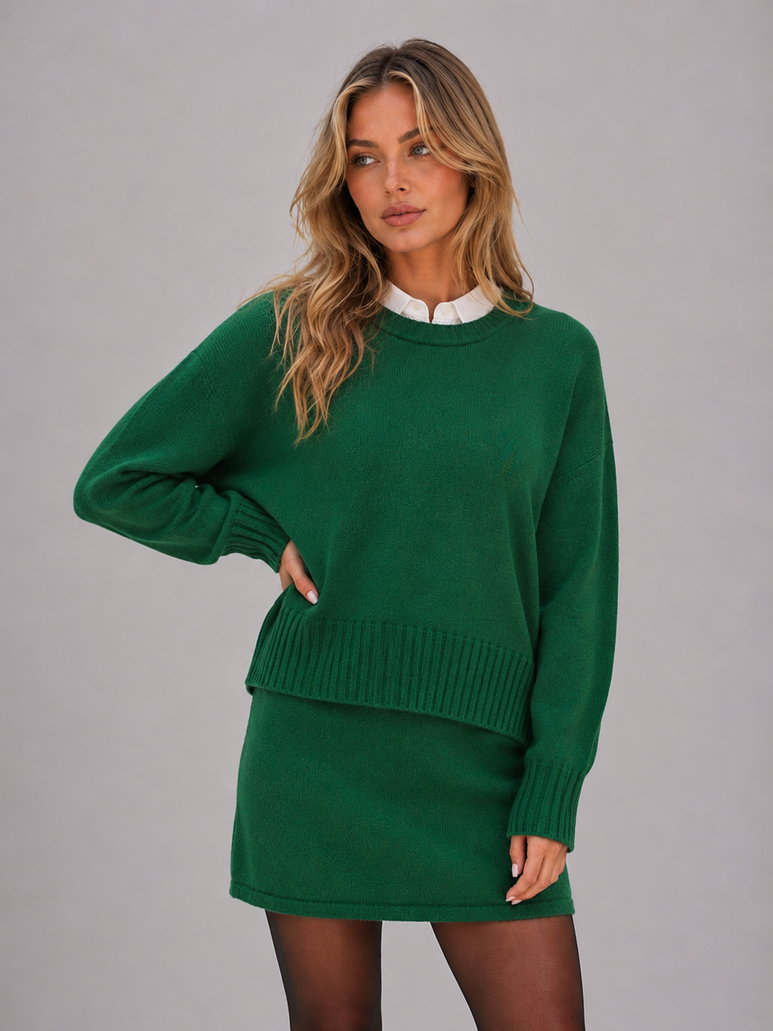 Woman wearing green knitted jumper with white collar and matching green mini skirt, styled with black tights against gray background