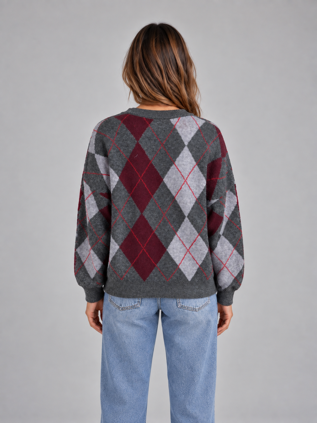 Woman wearing gray, burgundy and white argyle pattern crew neck knit jumper with long sleeves, styled with light blue jeans